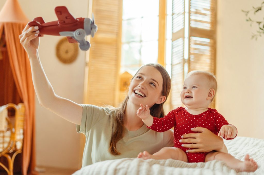 Happy mother playing with baby and toy airplane on bed
